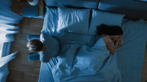 Depressed and Stressed Young Man Sits on the Edge of Bed at Night.